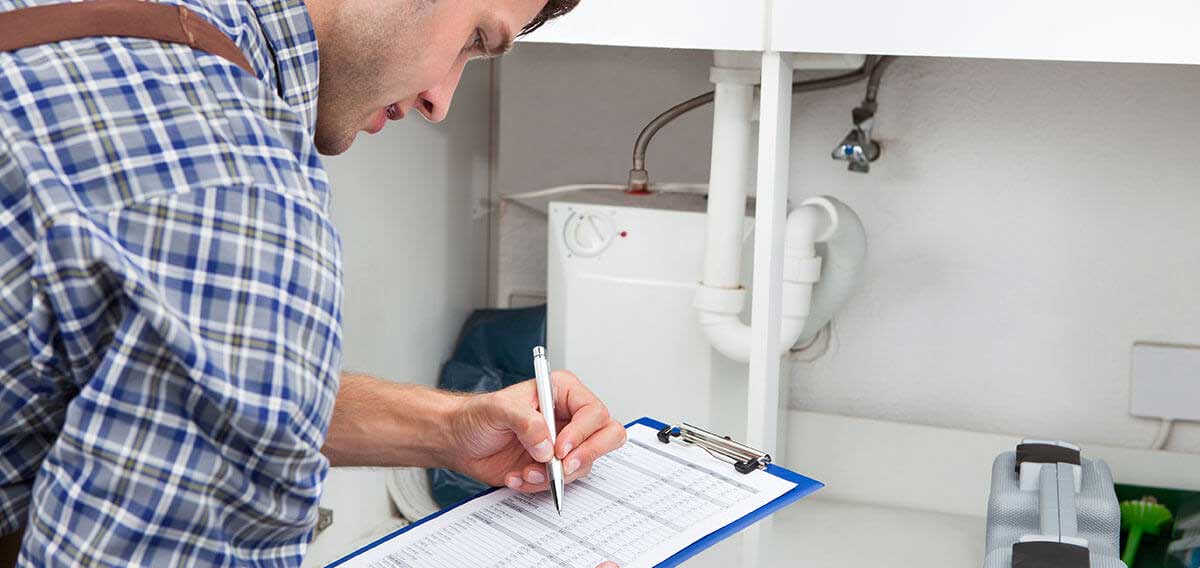 man with checklist on clipboard inspecting plumbing under the sink