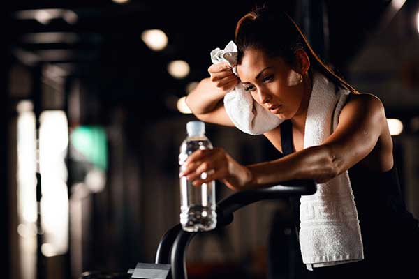 Woman holding a water bottle and wiping her brow with a towel after a tough workout.