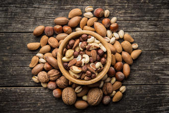 walnuts, pecans, almonds, peanuts, and other nuts in and around a bowl