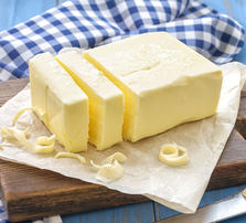 large block of butter with 2 sections cut on a wooden tray with gingham napkin