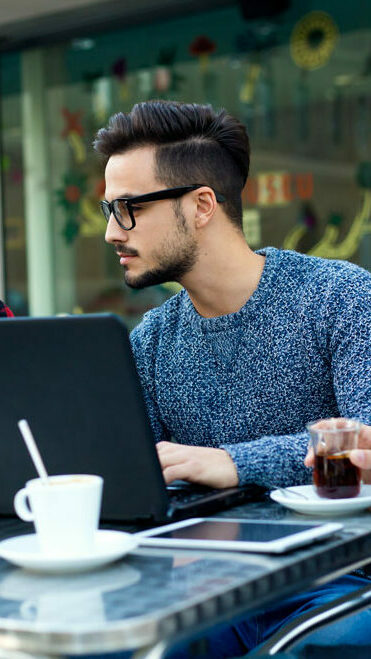 3 millennials at a cafe table working with laptop and tablet